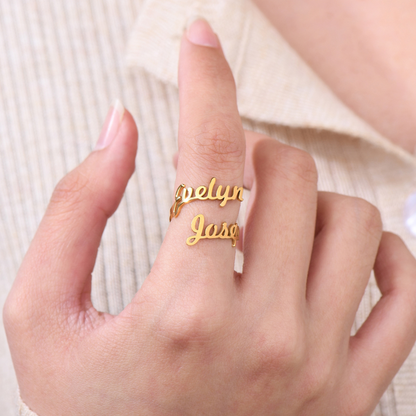 A gold ring featuring two names, "Evelyn" and "Jose," elegantly written in a cursive font. The names wrap around the finger, forming the band of the ring in a personalized, stylish design.