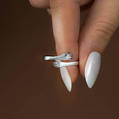 silver hug ring held by hand with white-colored manicure nails