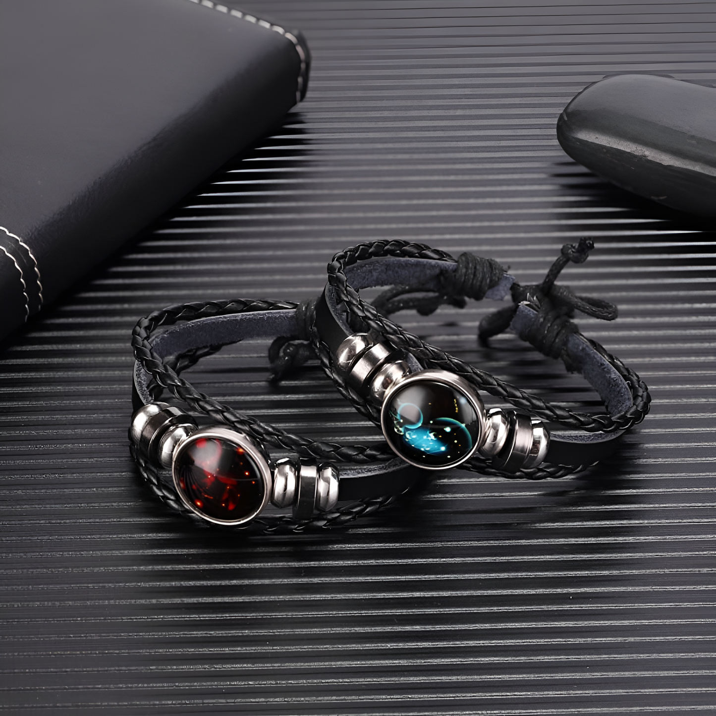 2 black leather braided bracelet with a circle pendant that has astrological symbols with a leather book cover, black stone on a black canvas