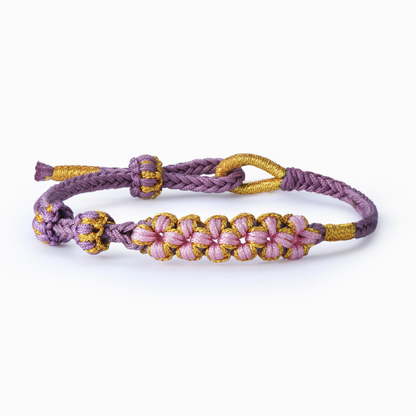 A purple and yellow braided leather bracelet with adjustable gold accent knots and a gorgeous pink and gold flower knots bead details.